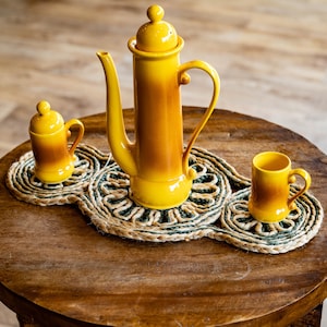 May include: A set of three yellow and brown ceramic kitchenware pieces, including a teapot, a sugar bowl, and a creamer, on a woven straw placemat.