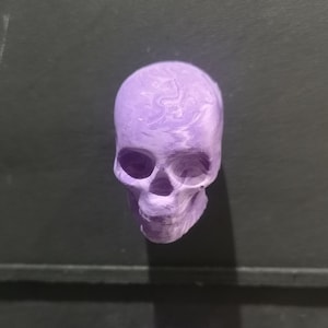 May include: A purple skull-shaped object with a marbled pattern. The skull is made of a smooth, hard material and has a slightly textured surface.