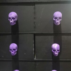 May include: Six purple skull drawer pulls with a marbled effect on a black dresser.