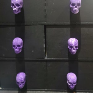 Peut inclure: Six tirettes de tiroir en forme de crâne violet sur une commode noire.