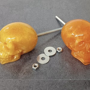 May include: Two orange skull-shaped cabinet knobs with silver metal hardware. The knobs are made of resin and have a glossy finish.