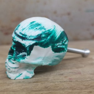Peut inclure: Bouton de porte en forme de crâne blanc avec un motif de peinture éclaboussée verte et noire. Le bouton a une vis en métal argenté.