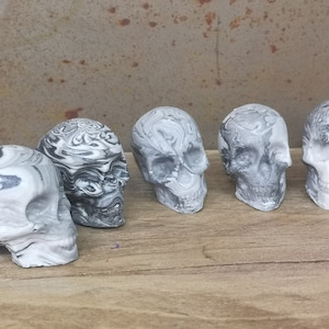 May include: Five small, white and black marbled skull figurines. The skulls are all facing forward and have a swirling pattern.
