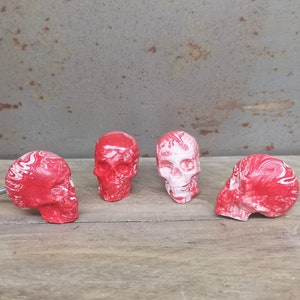 Peut inclure: Quatre poignées de tiroir en forme de crâne rouge et blanc avec un motif en spirale blanc. Les poignées sont en céramique et ont une finition mate.