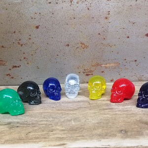 May include: A set of eight small, colorful skull figurines. The skulls are made of glass and are in various colors, including green, black, blue, clear, yellow, and red.