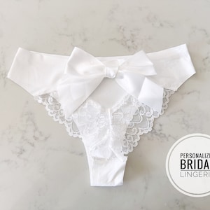 May include: White lace lingerie with a satin bow in the back. The text "Personalized Bridal Lingerie" is on a white circle.