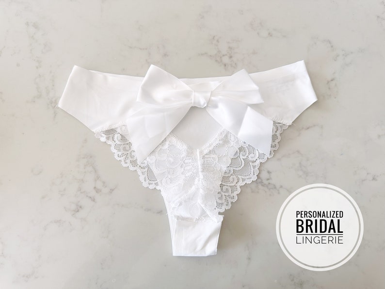 May include: White lace lingerie with a satin bow in the back. The text "Personalized Bridal Lingerie" is on a white circle.