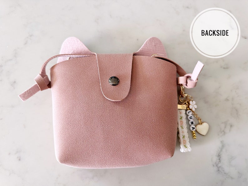 May include: A pink faux leather purse with cat ears and a gold chain with a charm that says "LUNA".