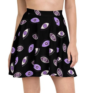 Puede incluir: Falda skater negra con un patrón repetido de ojos en tonos morados y blancos. La falda tiene una silueta acampanada y está hecha de una tela suave. El diseño es un patrón único y llamativo.