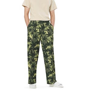 May include: A person wearing a light beige t-shirt and green camouflage pants with a leaf pattern. The pants have an elastic waistband.