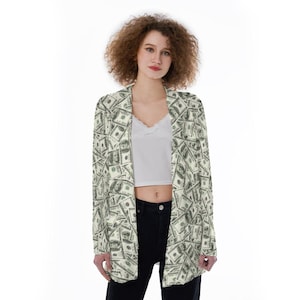 May include: A long-sleeved blazer with a pattern of US dollar bills. The blazer is light green and white with a subtle sheen. The blazer is open and the person wearing it is standing with their arms at their sides.