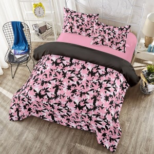 May include: A bed with a pink and black leaf-patterned duvet cover and pillowcases. The bed also has a pink sheet and a black comforter. The bed frame is white, and the room has a modern aesthetic.