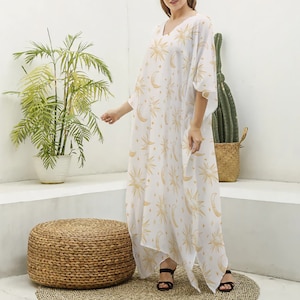 May include: White maxi dress with a gold and white sun and moon print. The dress has a V-neck and 3/4 sleeves.
