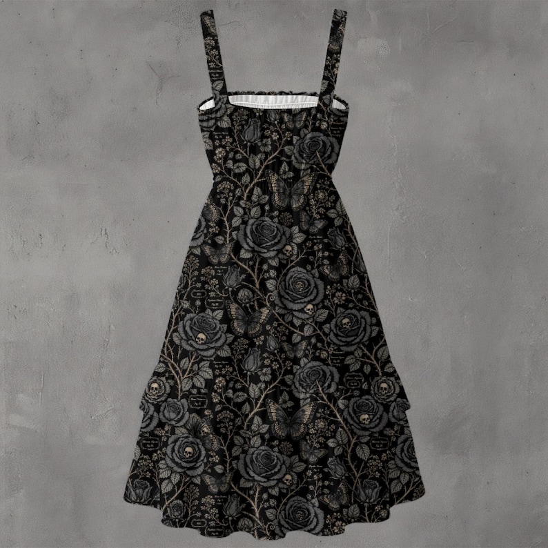 May include: A black sleeveless dress featuring a repeating pattern of grey roses, butterflies, and small skulls on a dark background. The dress has a square neckline with thin shoulder straps and a tiered skirt design that flares toward the hem.