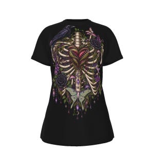 May include: A black t-shirt featuring a detailed graphic print of a human rib cage centred on the chest. The rib cage encloses a Venus flytrap heart, surrounded by a black raven, dark roses, small mushrooms, and a large pale green moth.