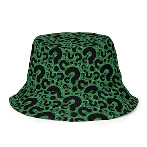 May include: A green bucket hat with a repeating pattern of black question marks. The hat has a glittery texture, adding a touch of sparkle. The hat's brim is curved, and the hat is designed to be worn on the head.