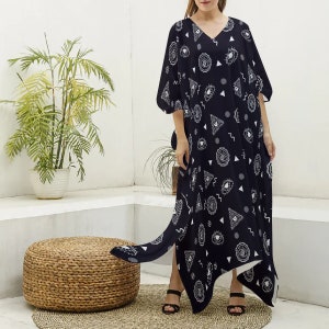 May include: A black maxi dress with a white eye and triangle pattern. The dress has a V-neckline and a long, flowing skirt. The dress is asymmetrical, with one side of the skirt being longer than the other.