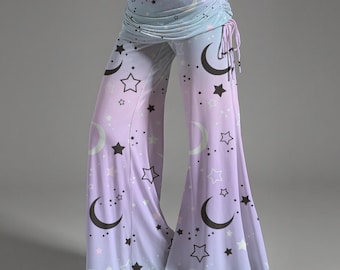 May include: Wide-leg pants with a celestial design. The pants feature a gradient of colors, transitioning from light blue to lavender. Black stars and crescent moons are scattered across the fabric. The waistband is ruched with a drawstring.