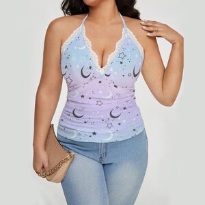 May include: A halter-style top with a celestial design. The top features a gradient of blue, purple, and white, adorned with crescent moons and stars. It has a lace trim and a wrap-style neckline.