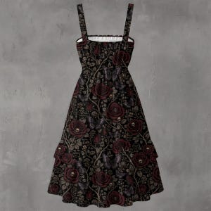 May include: A sleeveless midi dress featuring a black background with a repeating pattern of dark red roses, small skulls nestled within the flowers, and butterflies. The dress has a square neckline, thick shoulder straps, and a tiered skirt.
