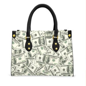 May include: A white handbag with a repeating pattern of $100 bills. The bag has a black handle and black accents. Gold-colored rivets secure the handle to the bag.