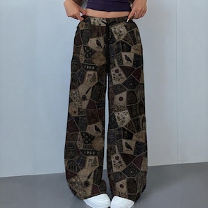 May include: Wide-leg pants featuring a dark, multi-patterned patchwork design in shades of brown, black, and tan. The fabric displays various motifs including crows, floral arrangements, and geometric shapes. The pants have a black drawstring waistband.