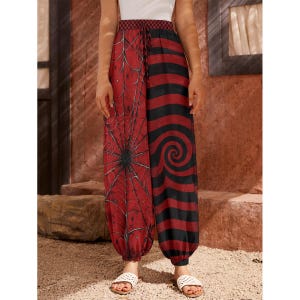 May include: High-waisted joggers featuring a split-leg design. One leg displays a black spiderweb pattern on a red background, while the other features alternating horizontal black and red stripes with a spiral graphic. Includes a drawstring waist.