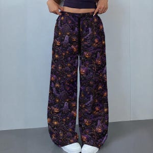 May include: Wide-leg trousers featuring a dark purple and black pattern with glowing orange jack-o'-lanterns, ghostly figures, and ornate lanterns. The pants have a high-waisted fit with a black drawstring closure at the center of the waistband.