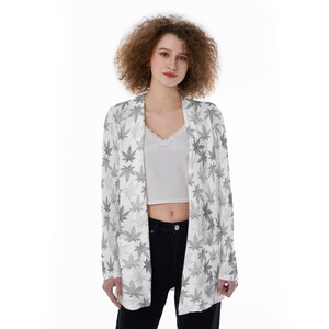 May include: A white cardigan with a gray leaf pattern. The cardigan has a long sleeve and a relaxed fit.