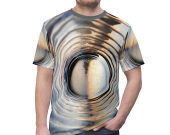 May include: A gray t-shirt with a swirling, abstract design featuring a large, round, metallic object in the center.