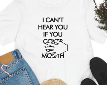 May include: White t-shirt with black text that reads "I can't hear you if you cover your mouth". A hand is shown covering its mouth.