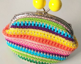 May include: A colorful crocheted coin purse with a rainbow striped pattern and a silver clasp. The purse has two yellow plastic balls on top of the clasp.