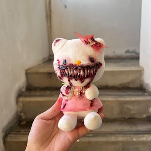 Puede incluir: Un peluche blanco, inspirado en un personaje de dibujos animados popular, pero con un tema de terror. Tiene un vestido rosa y un lazo rojo. La cara del personaje está modificada con una boca sangrienta y ojos oscuros, creando una estética espeluznante.