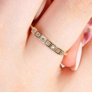 May include: A gold band ring with a row of small square-shaped diamonds.