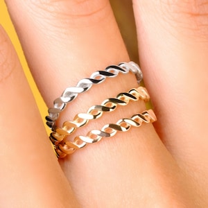 May include: Three gold and silver braided rings stacked on a finger.
