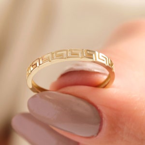 May include: A gold band ring with a geometric pattern. The ring is thin and delicate.