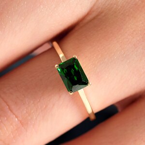 May include: A gold ring with a dark green emerald-cut gemstone.