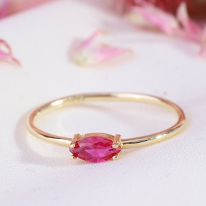 May include: A delicate gold ring with a single, marquise-shaped ruby gemstone set in the centre.