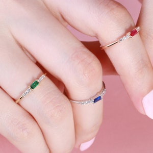 May include: Three gold rings with different colored gemstones. The rings are set with small diamonds and feature a single emerald, sapphire, and ruby gemstone.