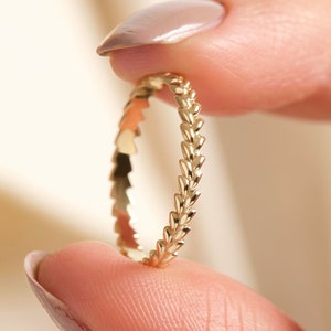 May include: A delicate gold ring featuring a textured, leaf-like design. The ring is thin and has a simple, elegant style.