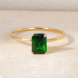 May include: A gold ring with a large emerald green rectangular gemstone.