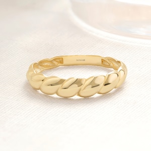 May include: A gold band ring with a twisted design. The inside of the band is marked "MINI14K".