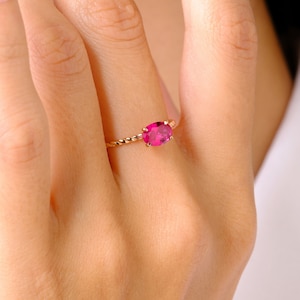 May include: A delicate gold ring with a twisted band and a pink oval gemstone.