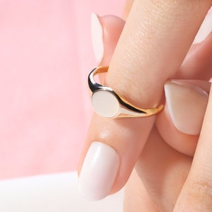 May include: A gold signet ring with a white oval stone on a finger with white nail polish.
