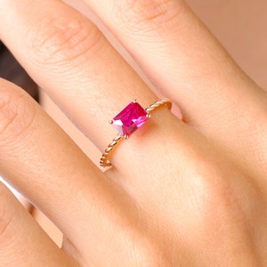 May include: A gold ring with a twisted band and a square-shaped, bright pink gemstone.