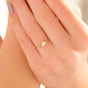 May include: A gold ring with a unique, abstract design. The ring is made of a smooth, polished metal and has a simple, modern style.
