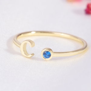 May include: A gold ring with a blue gemstone and a cut-out letter "C" on the band.