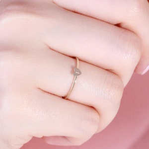May include: A gold ring with a small heart-shaped charm. The charm has a small letter 'I' engraved on it.