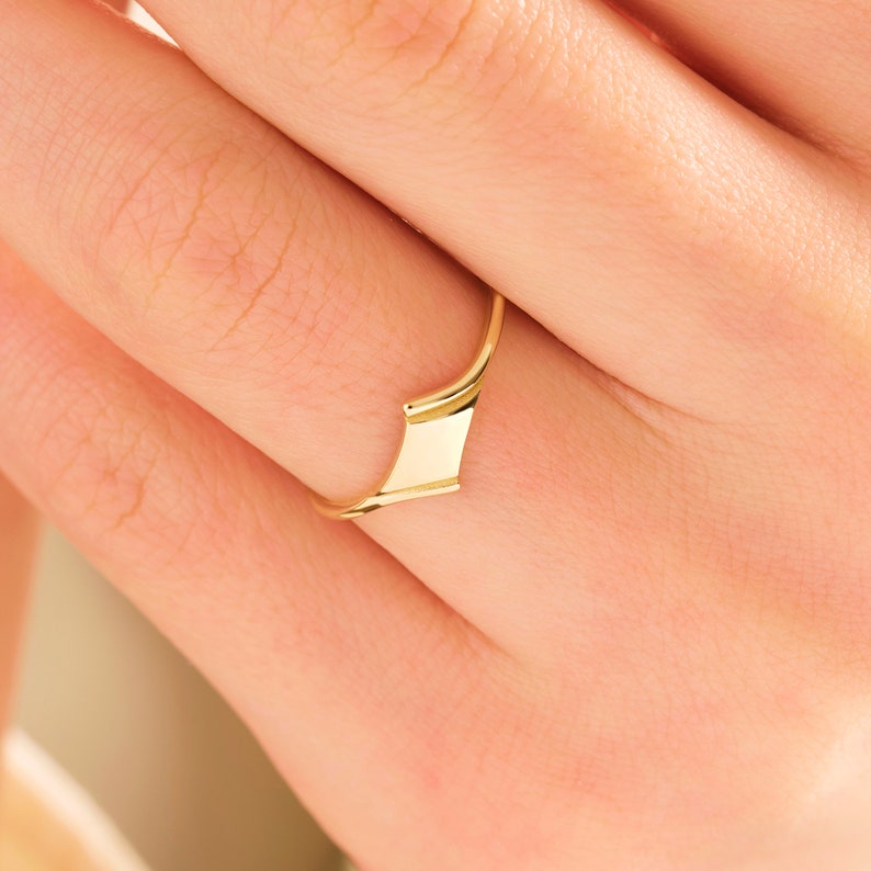 May include: A gold ring with a unique, angular design. The ring is worn on a finger.