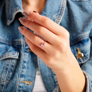 May include: A gold ring with three pink gemstones set in a row. The ring is on a person's finger.